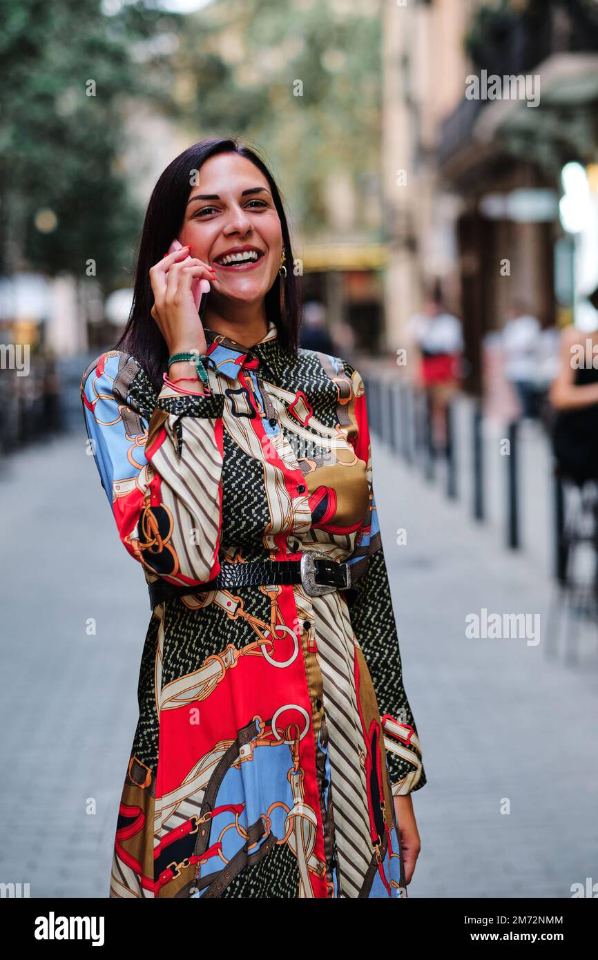 Stilvolle, glückliche Frau, die mit einem Handy auf der Straße spricht Stockfoto