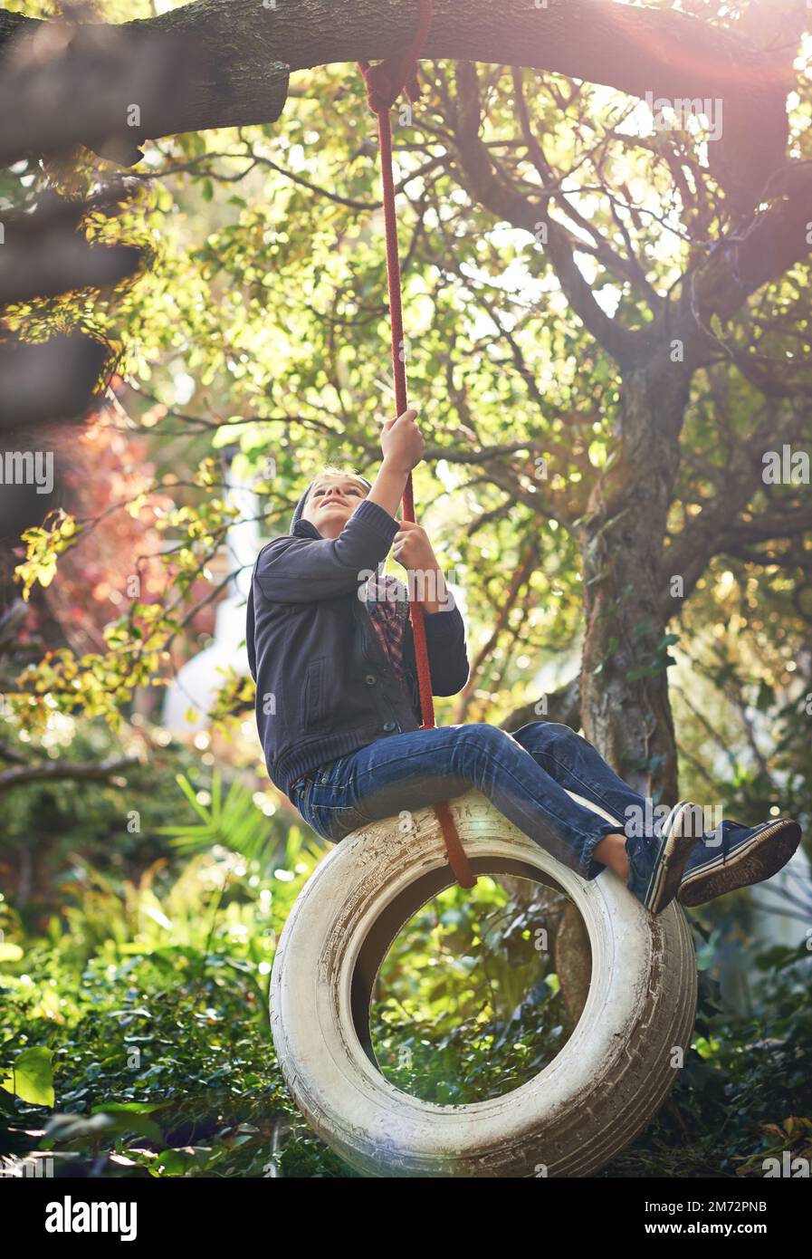 Das ist die ursprüngliche playstation. Ein junger Junge, der im Garten auf einer Reifenschaukel schwingt. Stockfoto