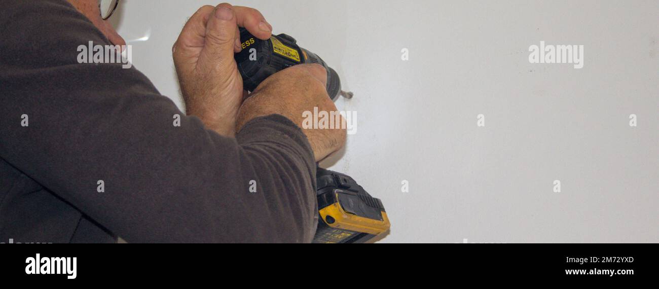 Bild eines Mannes, der mit einem Bohrer Löcher in eine Hauswand bohrt. Montage eines Regals an der Wand. Machen Sie es selbst. Horizontales Banner Stockfoto