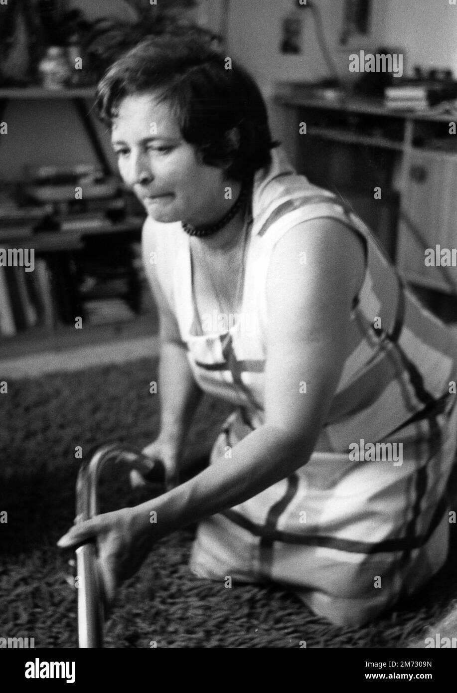 Eine 52-jährige Frau putzt den Boden auf ihren Knien mit einem Staubsauger Stockfoto