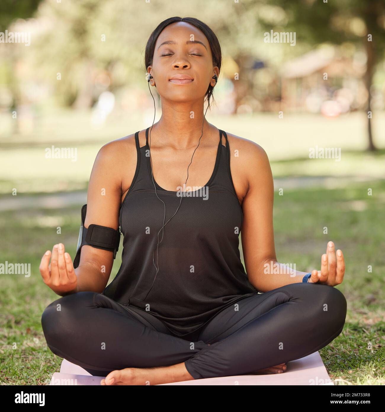 Yoga, Meditation schwarzer Frauen im Park mit Lotus-Pose, Kopfhörer für Achtsamkeit Podcast und Zen Outdoor in der Natur. Frieden, spirituelle Energie und Gleichgewicht Stockfoto
