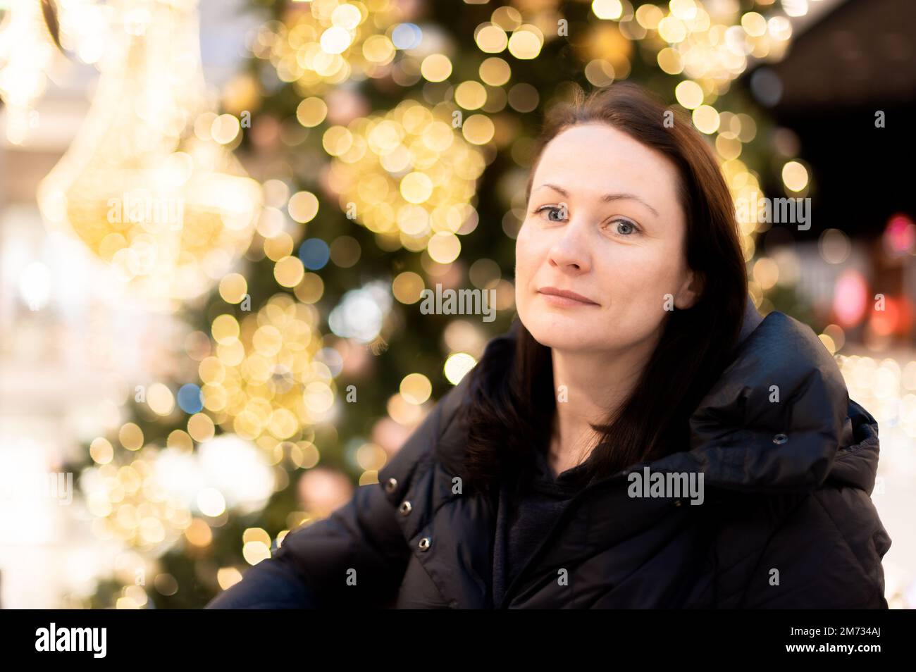 Porträt einer schönen Frau auf dem Hintergrund eines Weihnachtsbaums mit hellen Lichterkeimen. Wunderschönes bunten Bokeh im Hintergrund Stockfoto