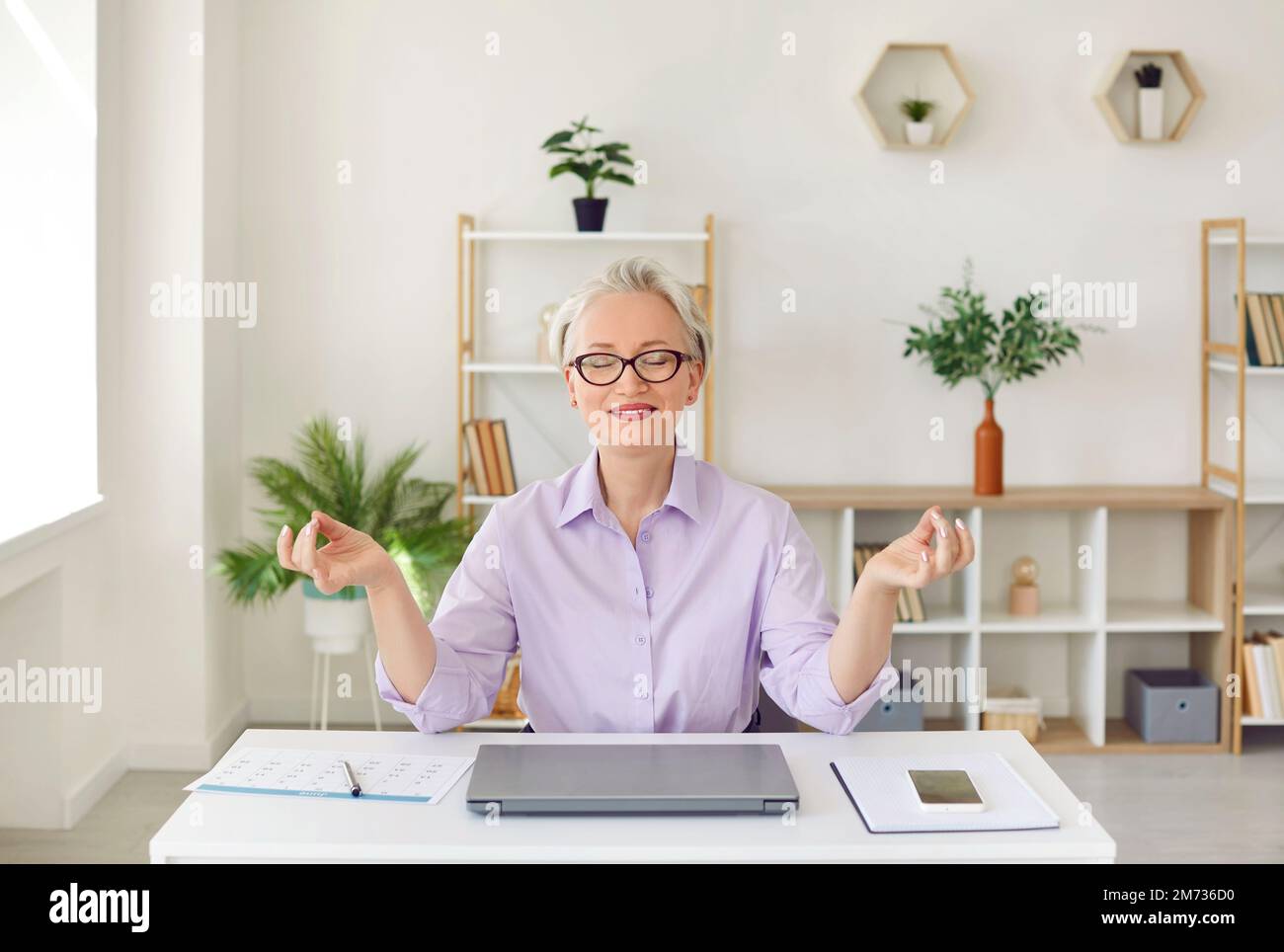 Friedliche, zufriedene Geschäftsfrau, die meditiert, während sie am Arbeitsplatz im Büro sitzt. Stockfoto