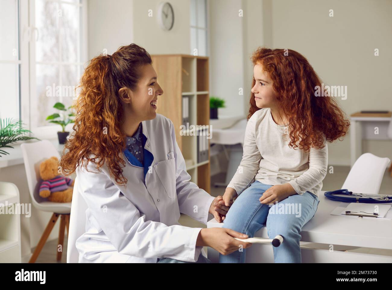 Eine Ärztin tippt das kleine Mädchen mit einem Spezialhammer auf das Knie, um ihre Reflexe zu überprüfen. Stockfoto