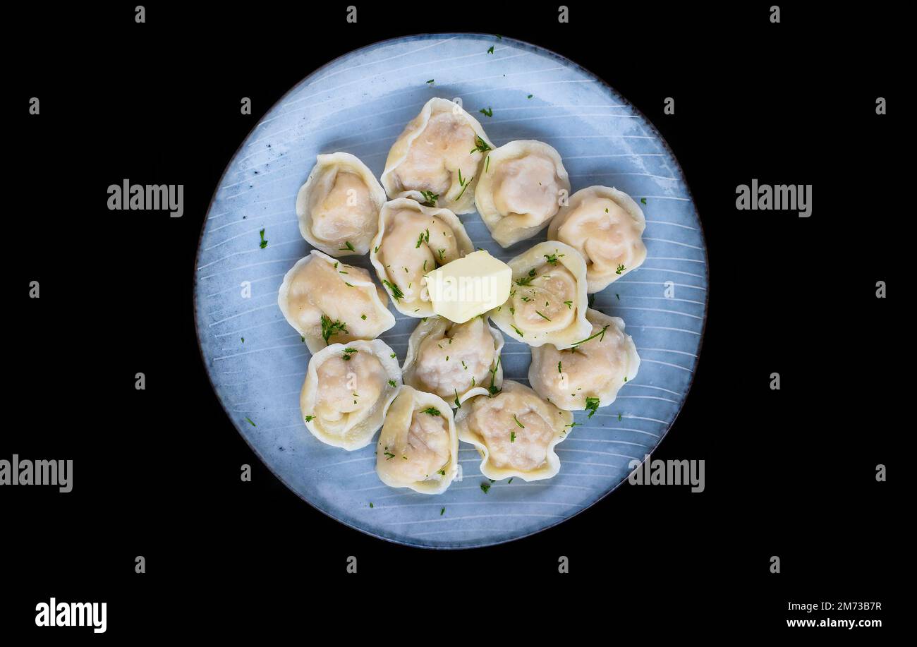 Russische Knödel pelmeni mit Butter auf schwarzem Hintergrund, Seitenansicht Stockfoto