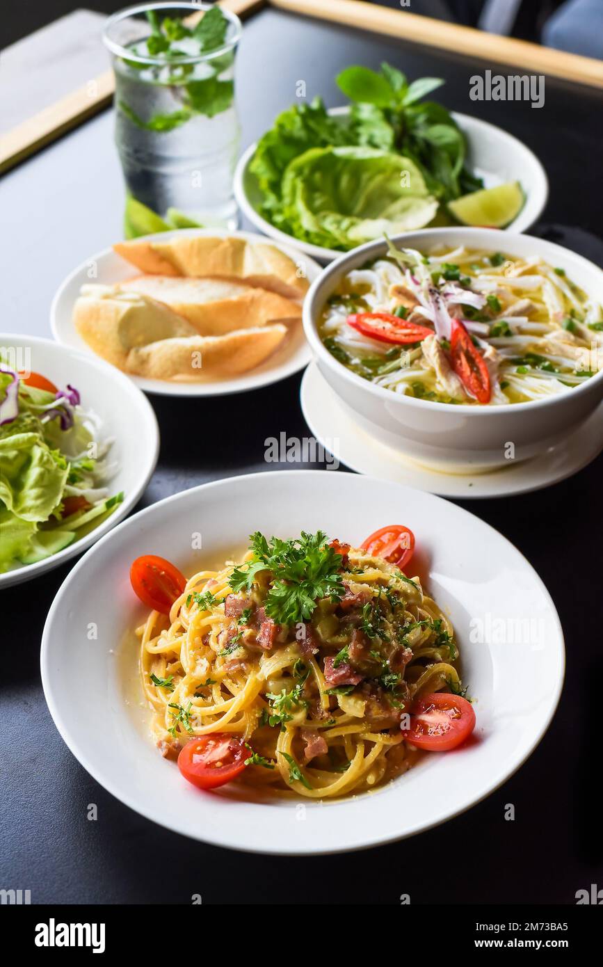 Mittagsset aus Hühnersuppe, Salat, Pasta Carbonara, Limonade auf schwarzem Hintergrund Stockfoto