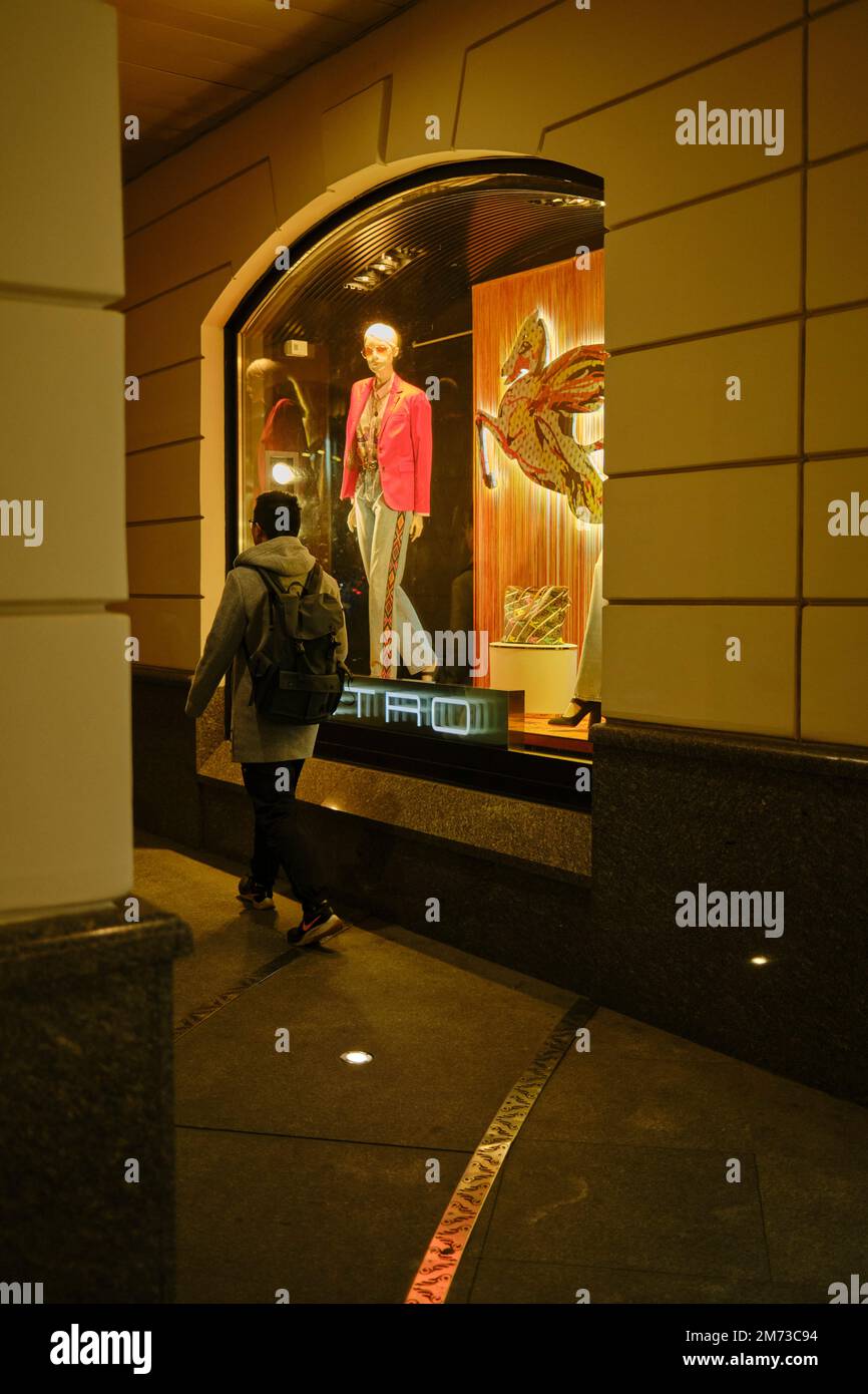 Ein junger Mann kommt an einem Schaufenster vorbei, das nachts hell beleuchtet ist. Moskau, Russland. Stockfoto