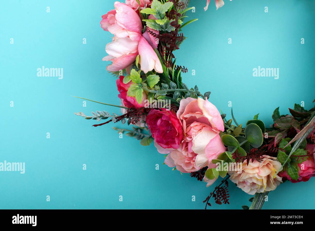 Farbenfroher künstlicher Blumenkranz isoliert auf hellaquagrünem Hintergrund Stockfoto