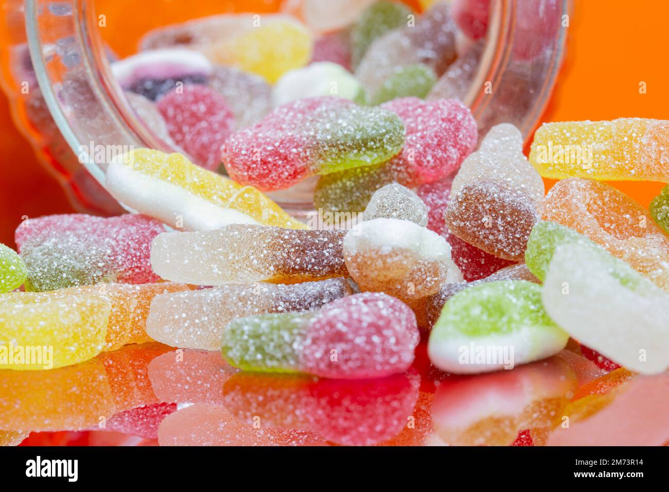 Mischung aus zuckerbeschichteten Süßigkeiten Süßigkeiten Süßigkeiten in einem Glasgefäß. Auf orangefarbenem Hintergrund Stockfoto