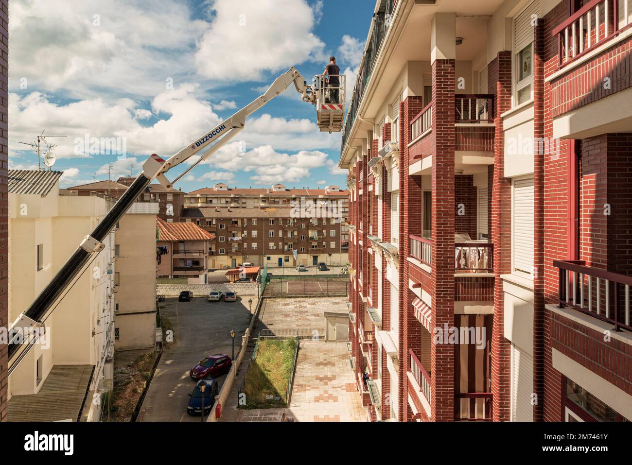 Arbeiter auf einem Kran mit Hebekorb repariert die Wand des Gebäudes. Der Baumeister in der hydraulischen Hebebühne reinigt die Dachrinne der Fassade. Stockfoto