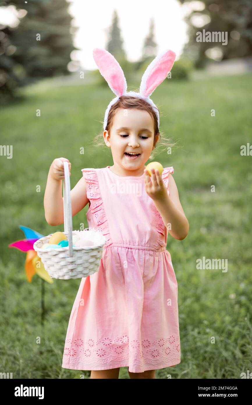 Das kleine süße Mädchen trägt bei der Ostereiersuche im Park einen Korb mit bunten Eiern. Stockfoto