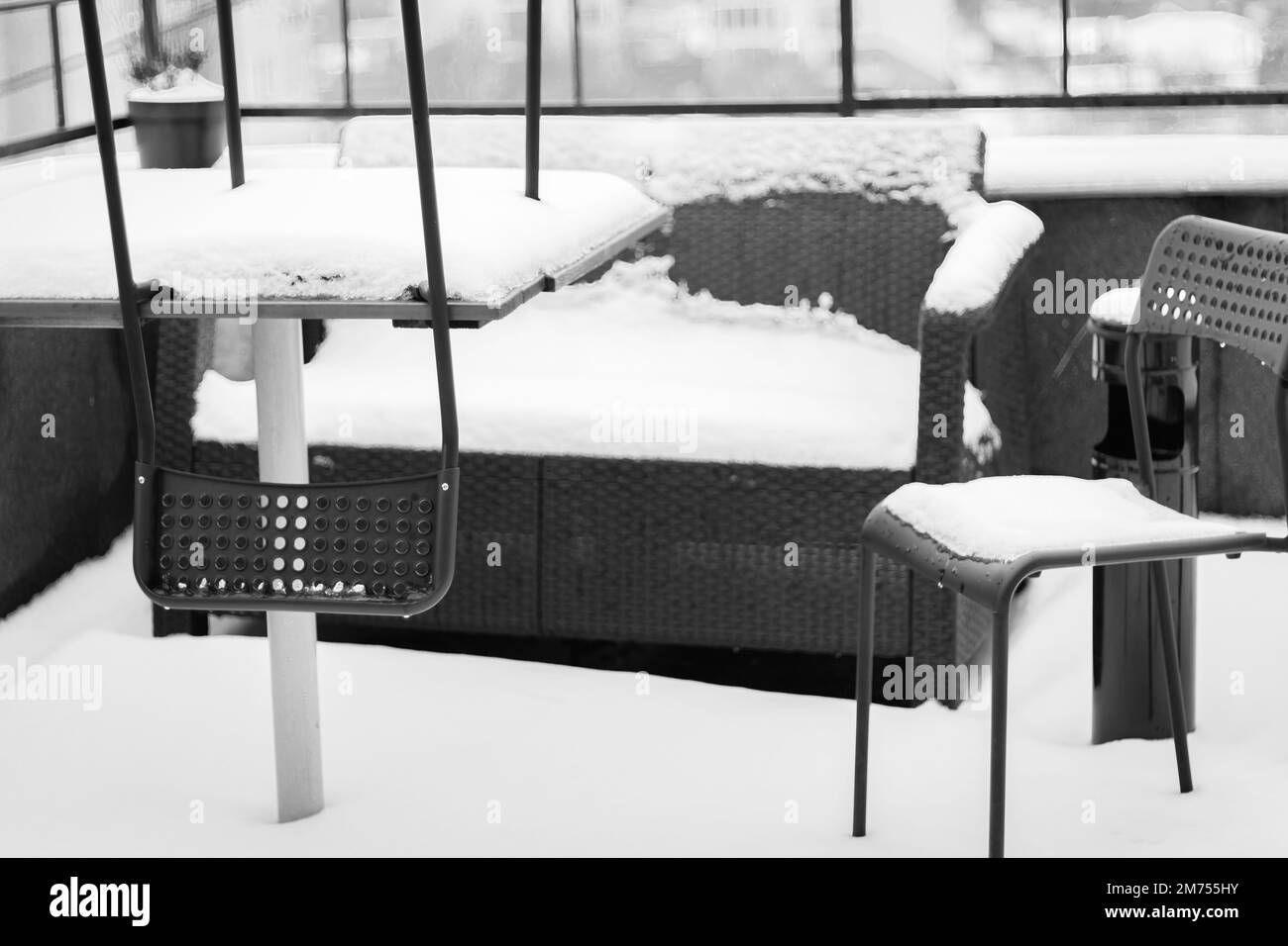 Schneebedeckte Gartenmöbel in Schwarz und Weiß. Schneebedeckte Stühle und Sofa auf dem Balkon. Winter in der Stadt. Stadt bedeckt mit frischem Schnee. Stockfoto