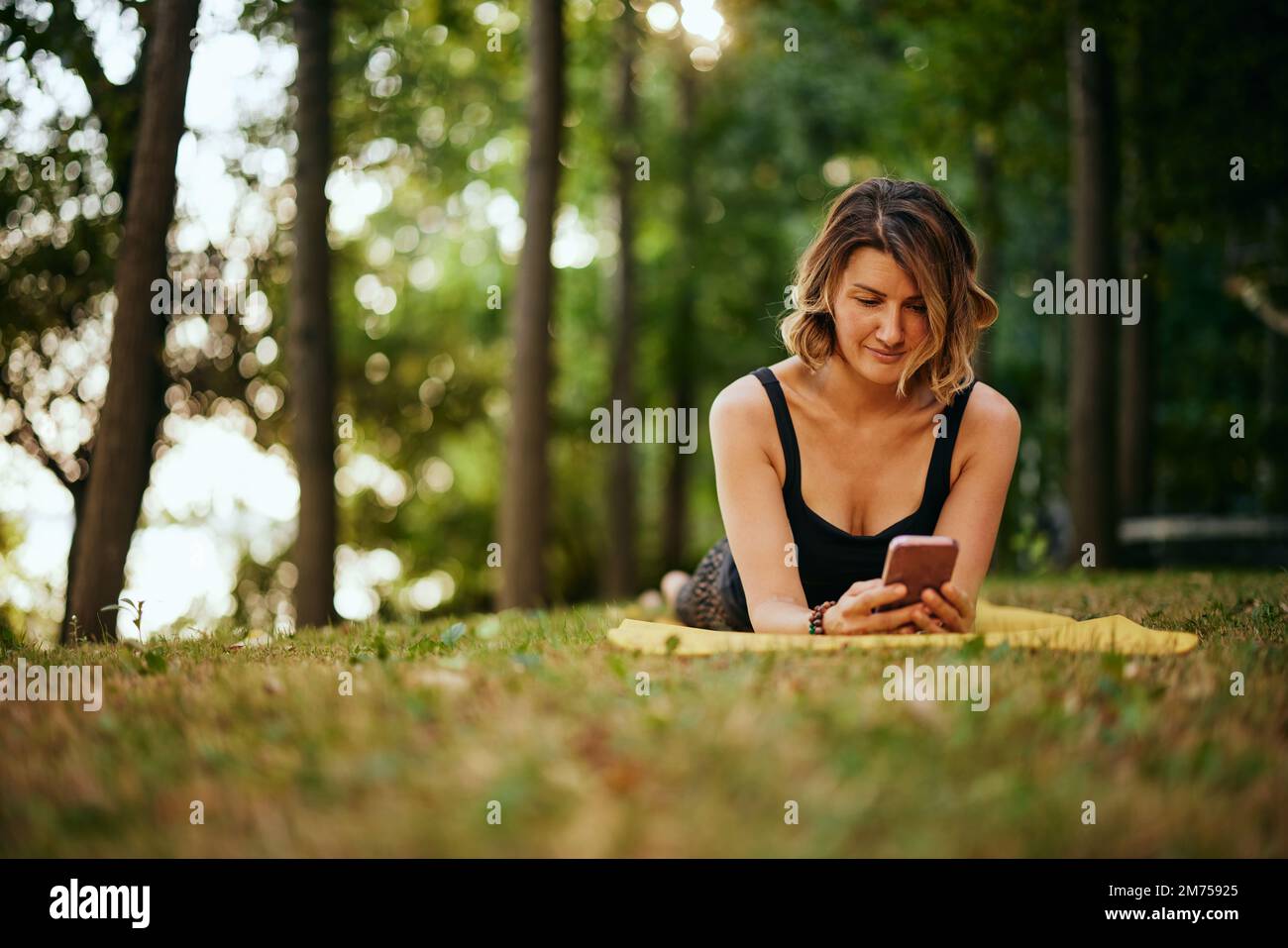 Eine gesunde Yoga liegt im Wald auf dem Bauch und telefoniert. Stockfoto
