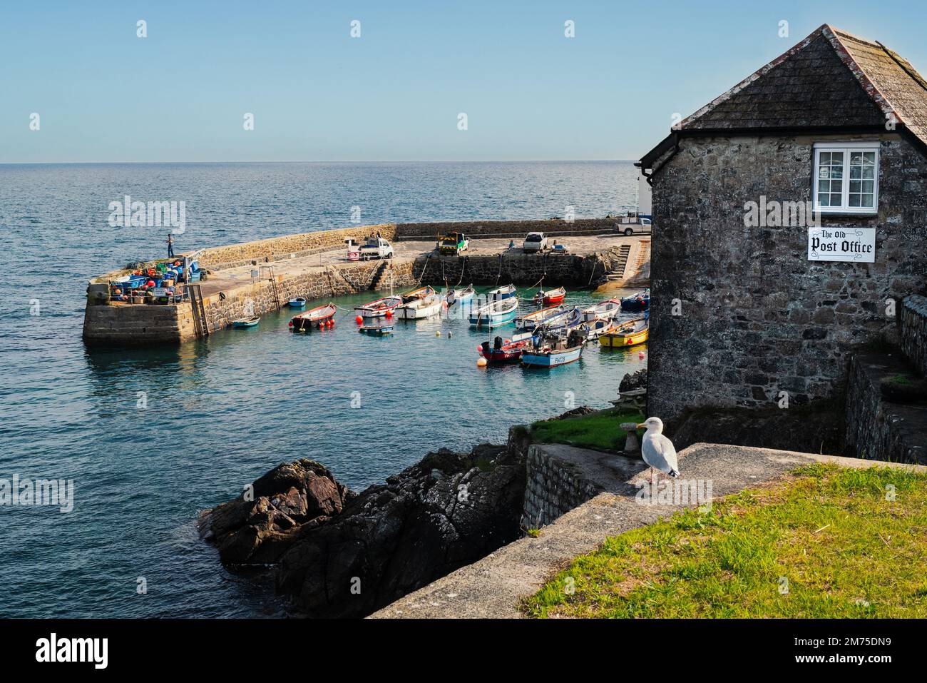 Coverack, Großbritannien - Okt. 3 2022. Kleine Fischerboote im Hafen von Coverack. Das alte Postamt und eine Heringsmöwe sind im Vordergrund. Stockfoto