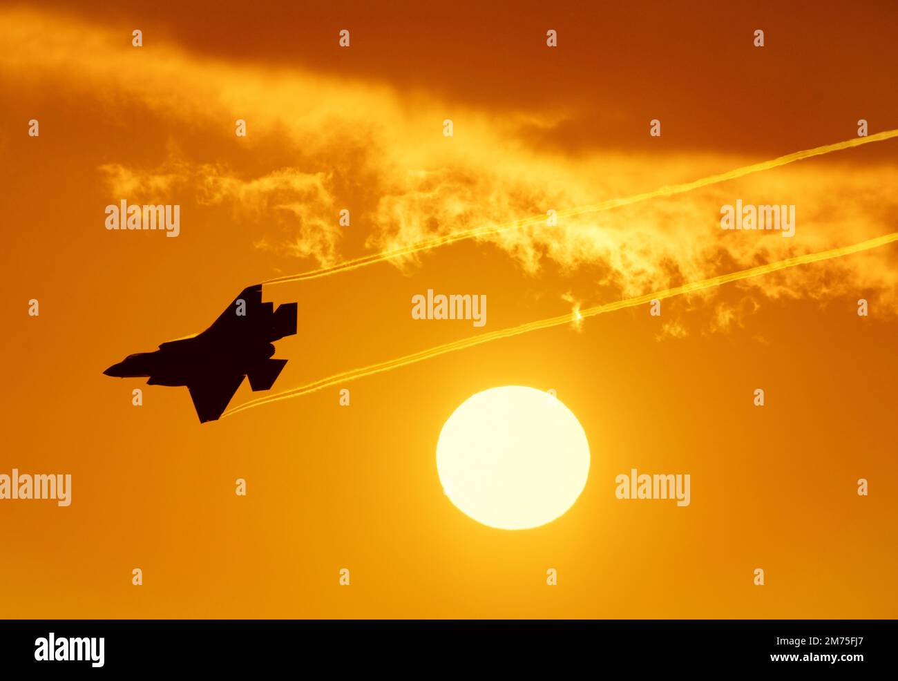 Kampfjet bei Sonnenuntergang. Moderner militärischer Kampfflugjet der fünften Generation, der Dampf an der untergehenden Sonne vorbeiströmt. Kampfflugzeuge mit orangefarbenem Himmel Stockfoto