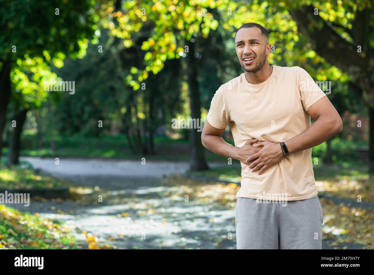 Der lateinamerikanische Läufer Sportler hat starke Bauchschmerzen, der Mann hält die Hand an der Seite des Magens, nachdem er im Park draußen trainiert und trainiert hat. Stockfoto