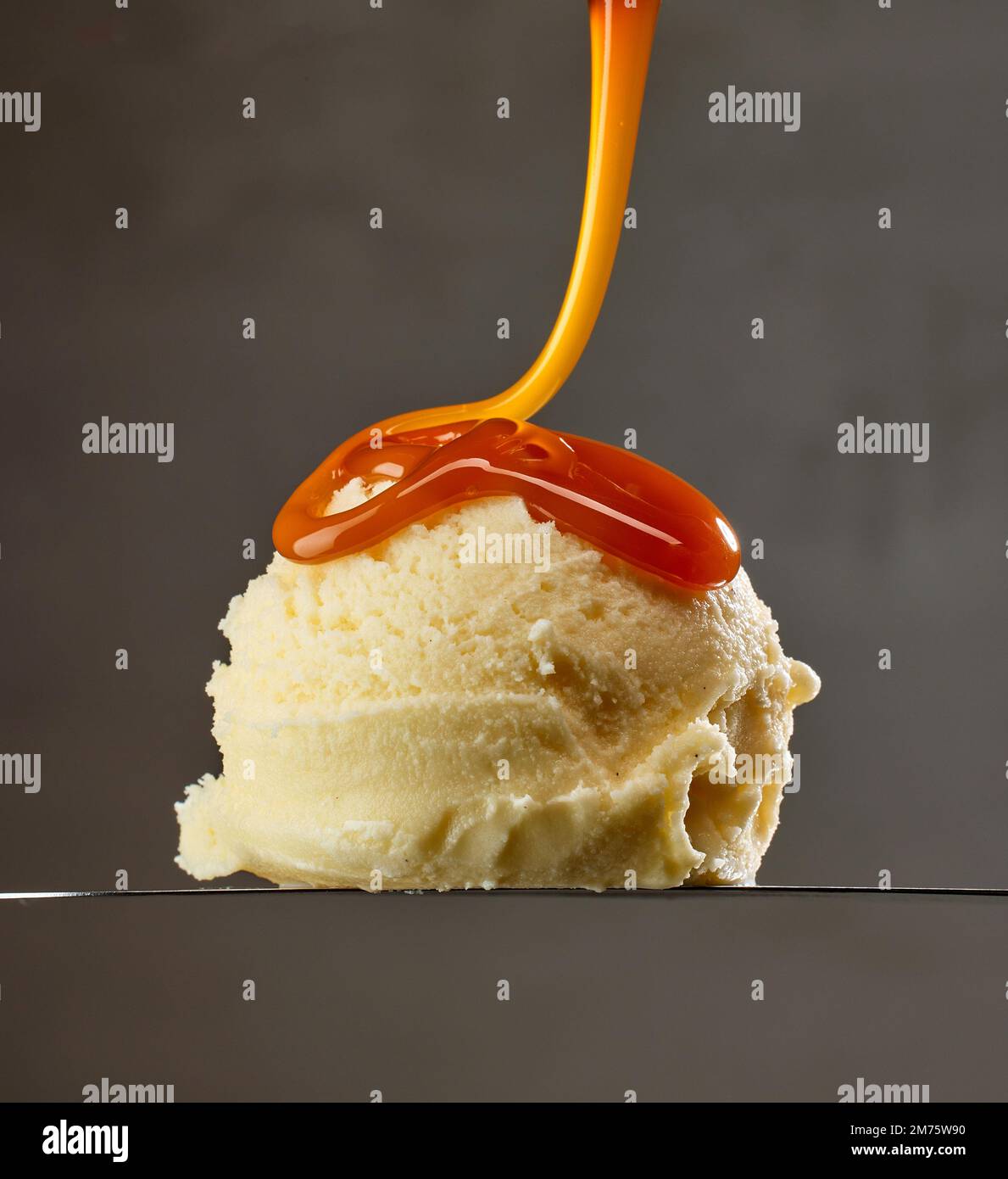 Vanille-Eiskugel mit Karamellsauce auf grauem Hintergrund Stockfoto