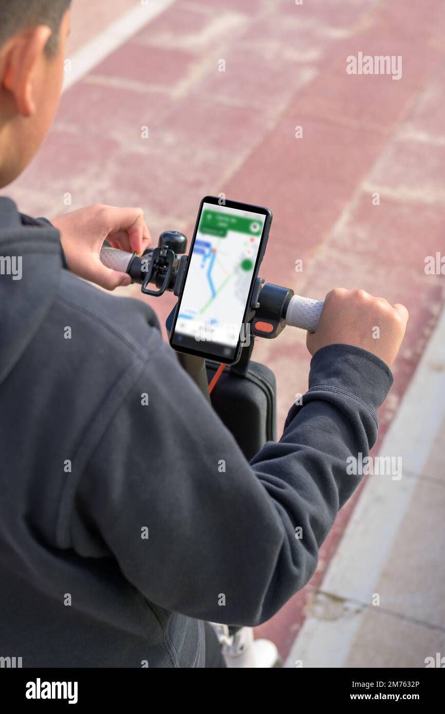 Junger Mann, der im Freien auf einem elektrischen Skateboard fährt, sich die Route auf einer Smartphone-Kartenanwendung ansieht, ein nachhaltiges Verkehrskonzept, CO2-emissionsfrei Stockfoto