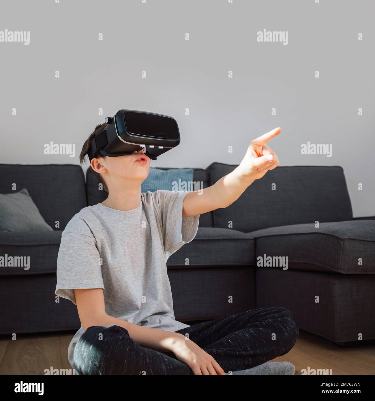 Ein Junge im kaukasischen Schulalter genießt zu Hause neue Technologie, verwendet VR-Brillen und interagiert mit Objekten in einer virtuellen Welt Stockfoto