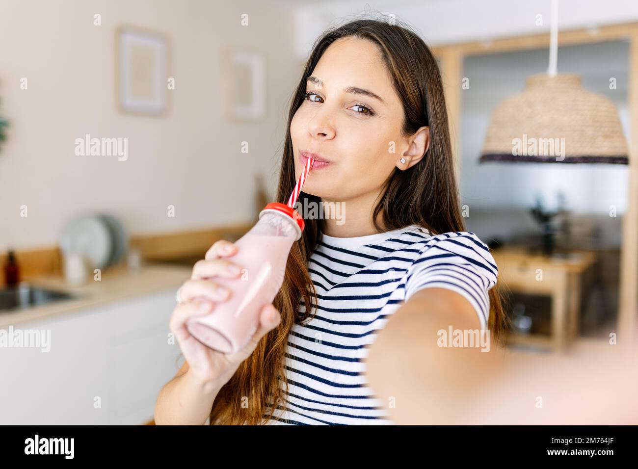Fröhliche junge Erwachsene Frau, die Selfie nimmt, während sie gesunden Fruchtsaft trinkt Stockfoto