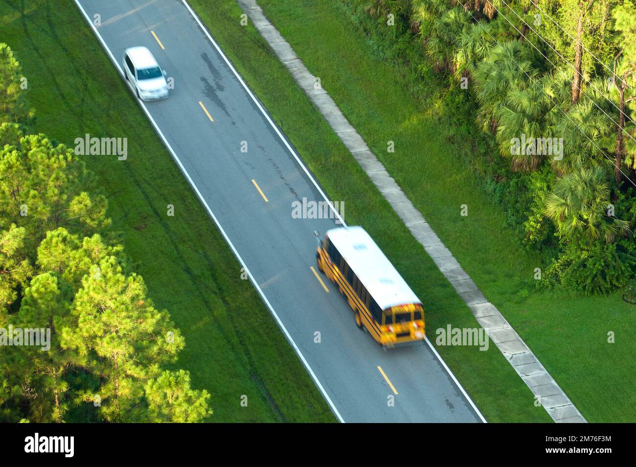 Draufsicht auf den klassischen gelben schulbus der usa, der auf der Straße der ländlichen Stadt fährt, um Kinder für ihre kleinen Kinder am frühen Morgen abzuholen. Öffentlich Stockfoto
