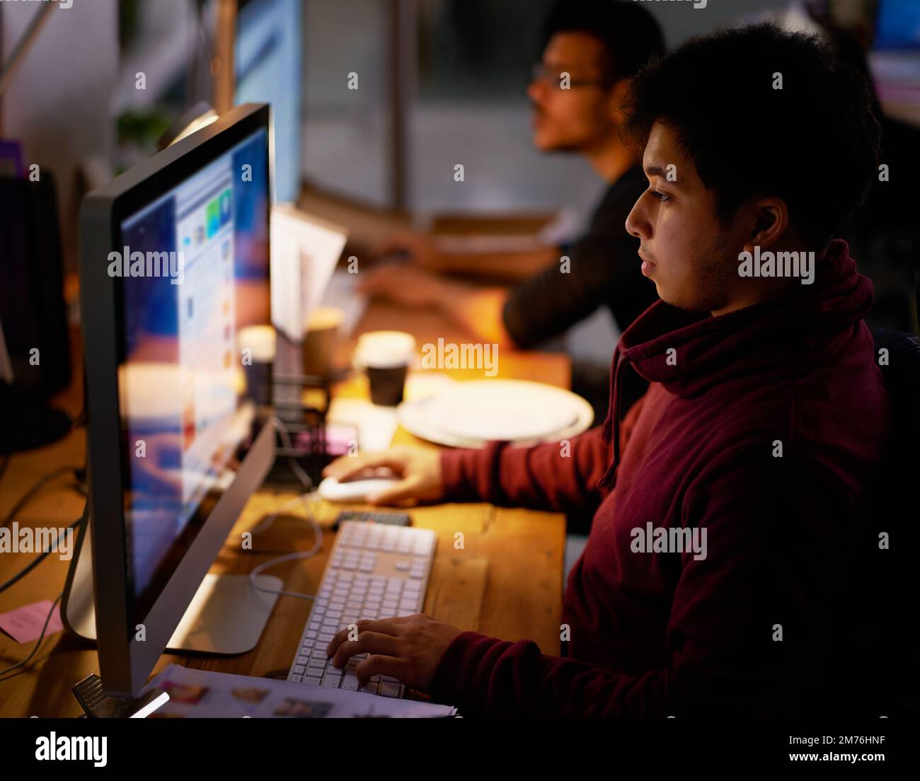 Eine Gruppe junger Mitarbeiter, die in einem schwach beleuchteten Büro arbeiten. Stockfoto
