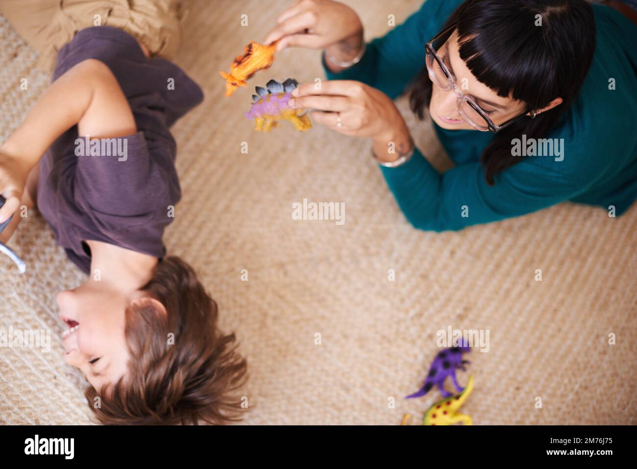 Sie weiß, wie man ihn zum Lächeln bringt. Eine Mutter und ihr Sohn, die mit Spielzeugdinosauriern spielen. Stockfoto