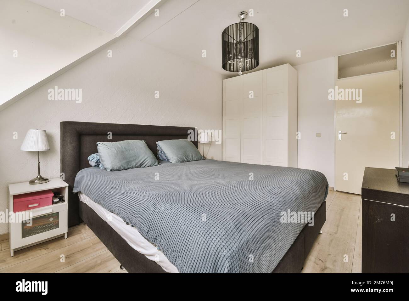 Ein Schlafzimmer mit einem Bett, Kommode und Spiegel an der Wand vor dem  Bett, es gibt eine Lampe über dem Bett Stockfotografie - Alamy
