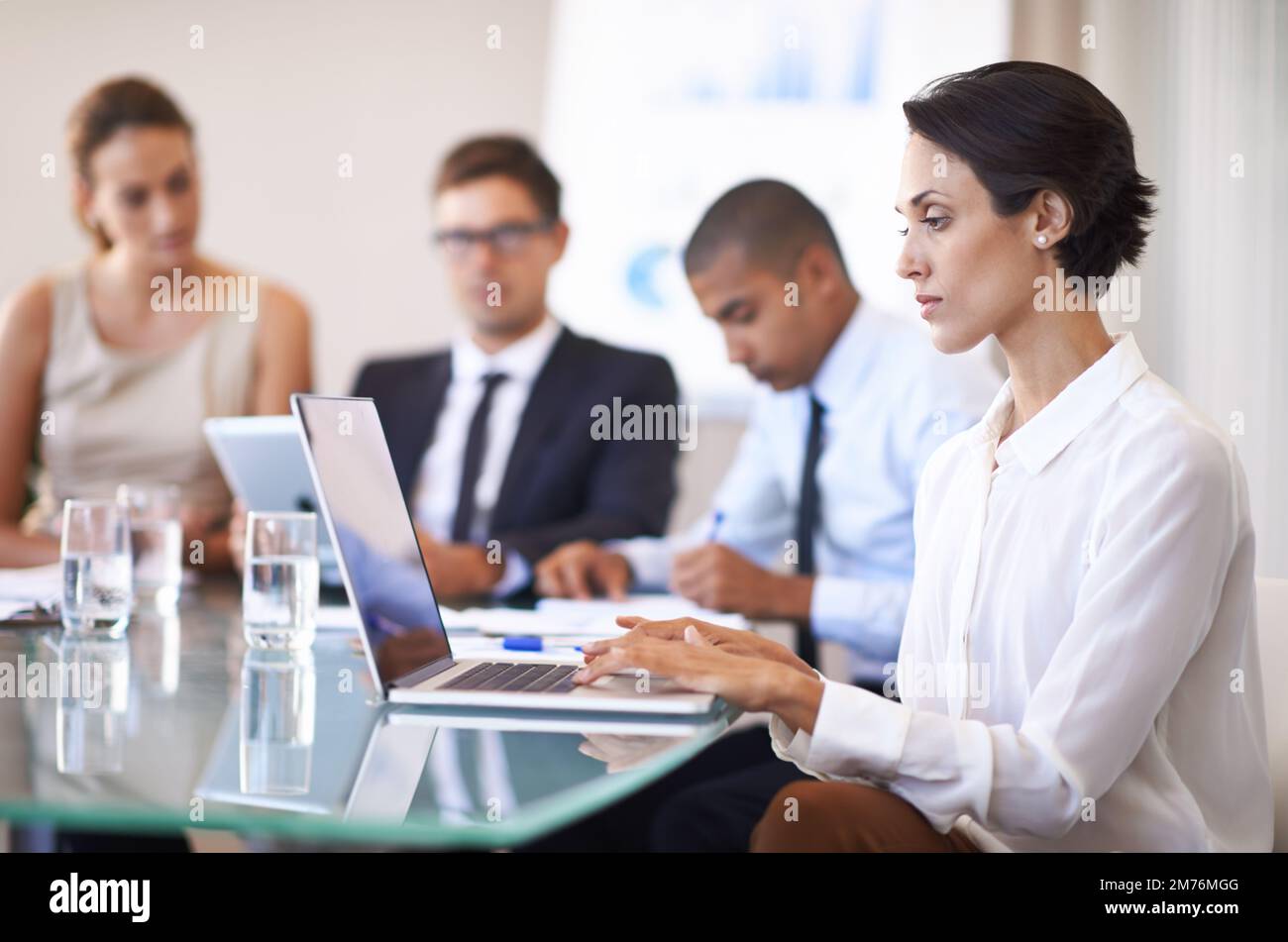 Sie ist immer voll konzentriert. Eine Geschäftsfrau, die vor ihren Kollegen ein Notebook verwendet. Stockfoto