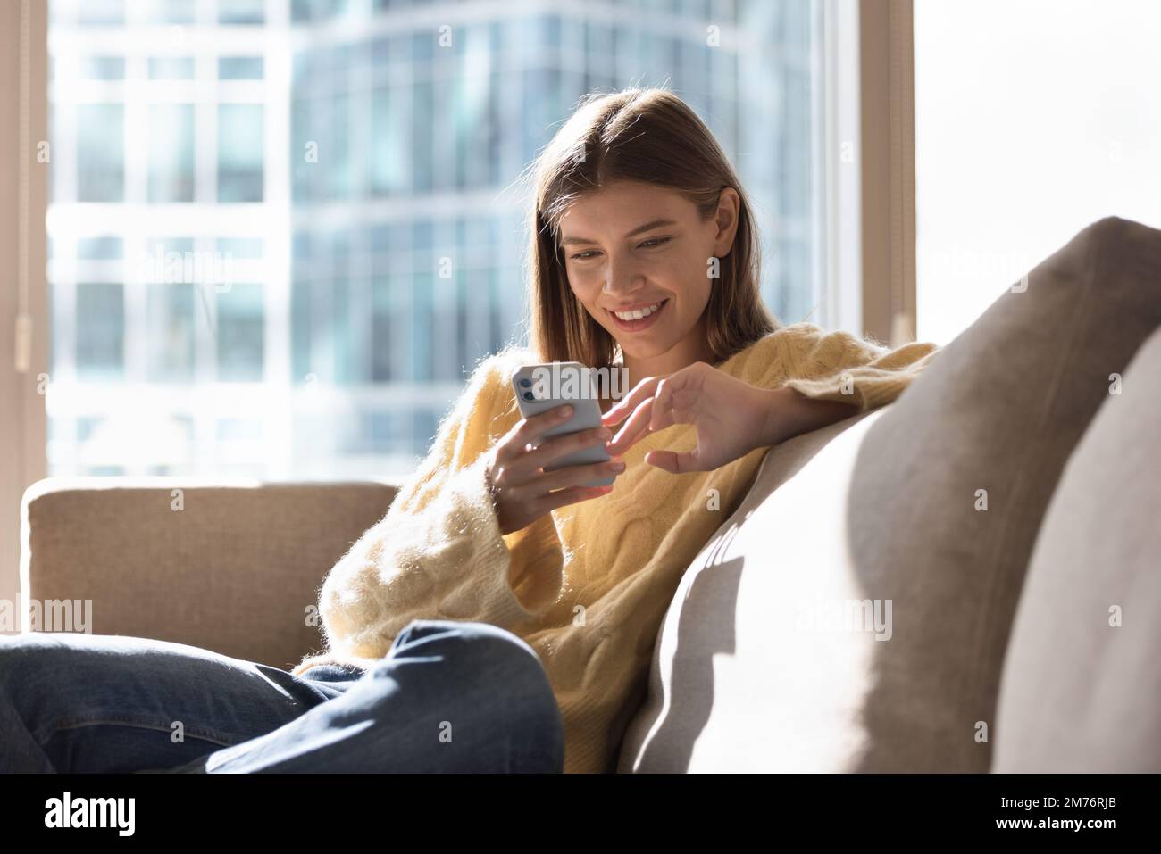 Schöne junge Frau, die auf dem Sofa ruht, benutzt ein Handy Stockfoto