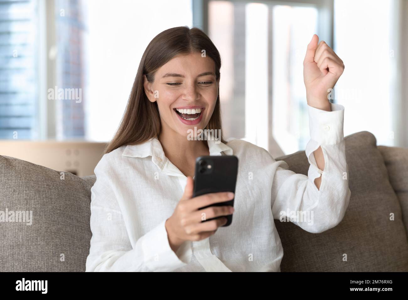 Die Frau, die auf den Handybildschirm schaut und tolle Nachrichten liest, fühlt sich glücklich an Stockfoto