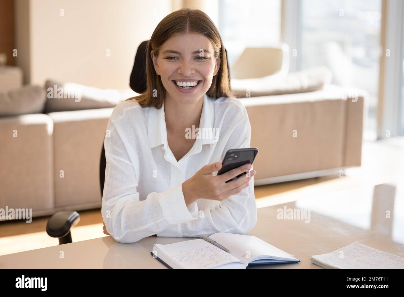 Eine lachende Frau mit Smartphone sitzt am Schreibtisch mit einem persönlichen Organizer Stockfoto