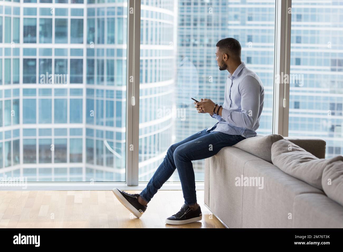 Ein afrikanischer Geschäftsmann hält sein Smartphone und schaut auf städtische Großbauten Stockfoto