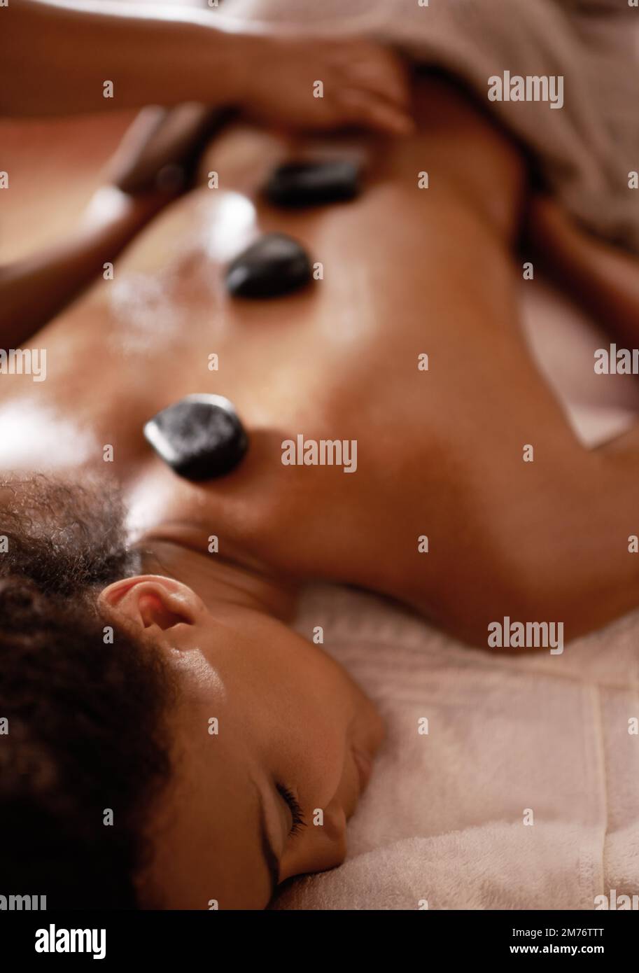 Stöcke und Steine werden diese Knochen heilen... eine junge Frau, die eine Hot-Stone-Therapie in einem Spa genießt. Stockfoto