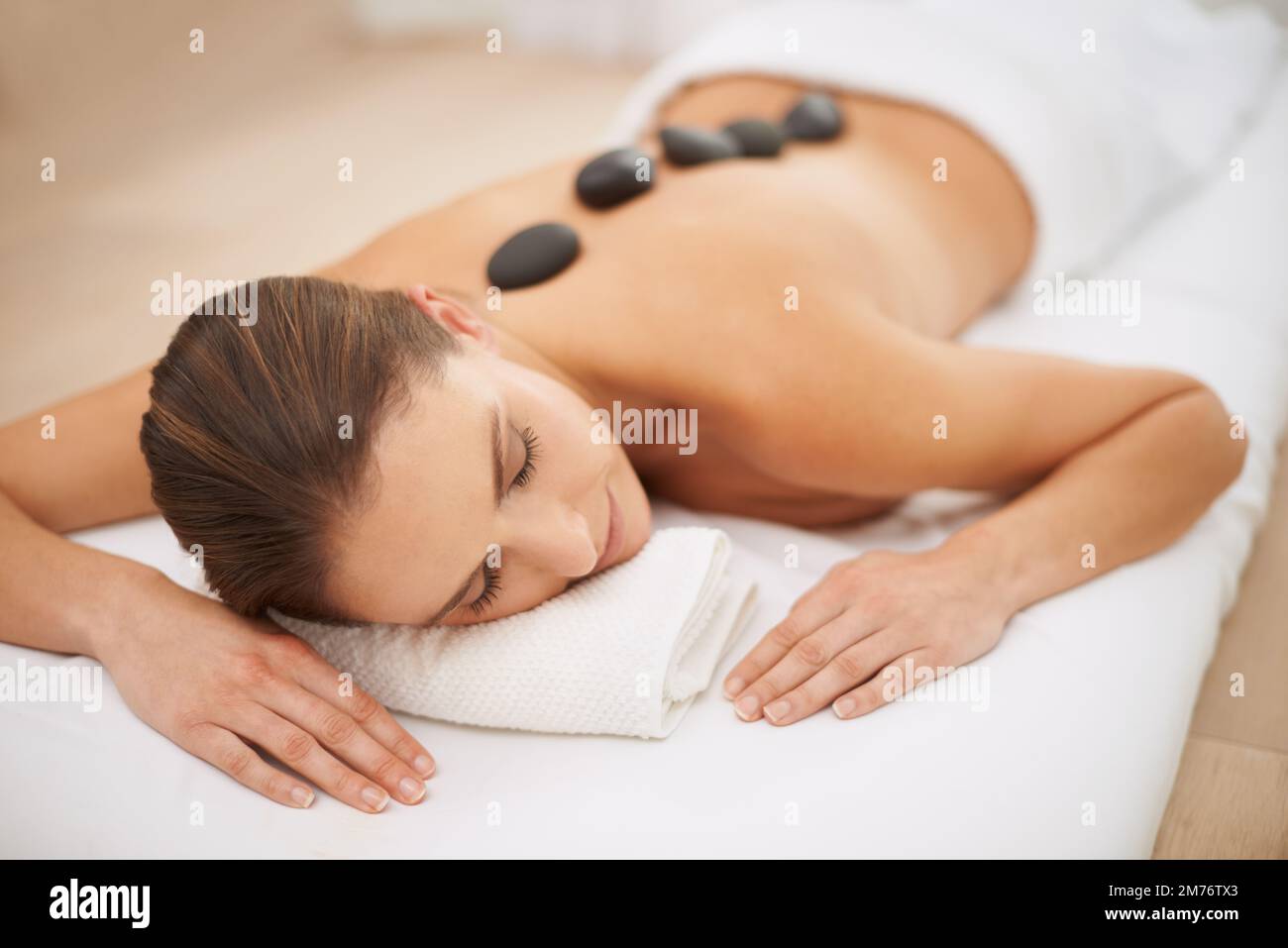 Entspannen Sie sich bei einer Hot-Stone-Massage. Eine wunderschöne junge Frau, die eine Hot-Stone-Massage genießt. Stockfoto