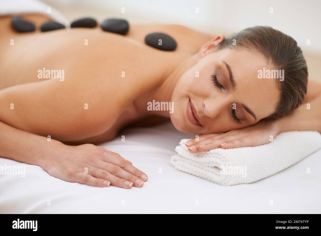 Im Spa stoned zu werden. Eine wunderschöne junge Frau, die eine Hot-Stone-Massage genießt. Stockfoto