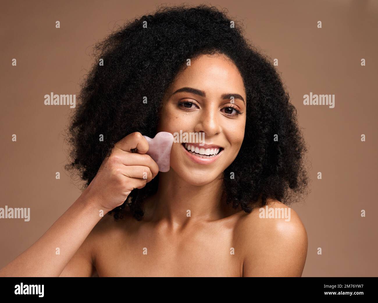 Frau, Studioporträt und Crystal guasha für Hautpflege, Lächeln oder kosmetische Gesichtsmassage im Hintergrund. Schwarze Frau, Model und Selbsthilfe mit Rose Stockfoto