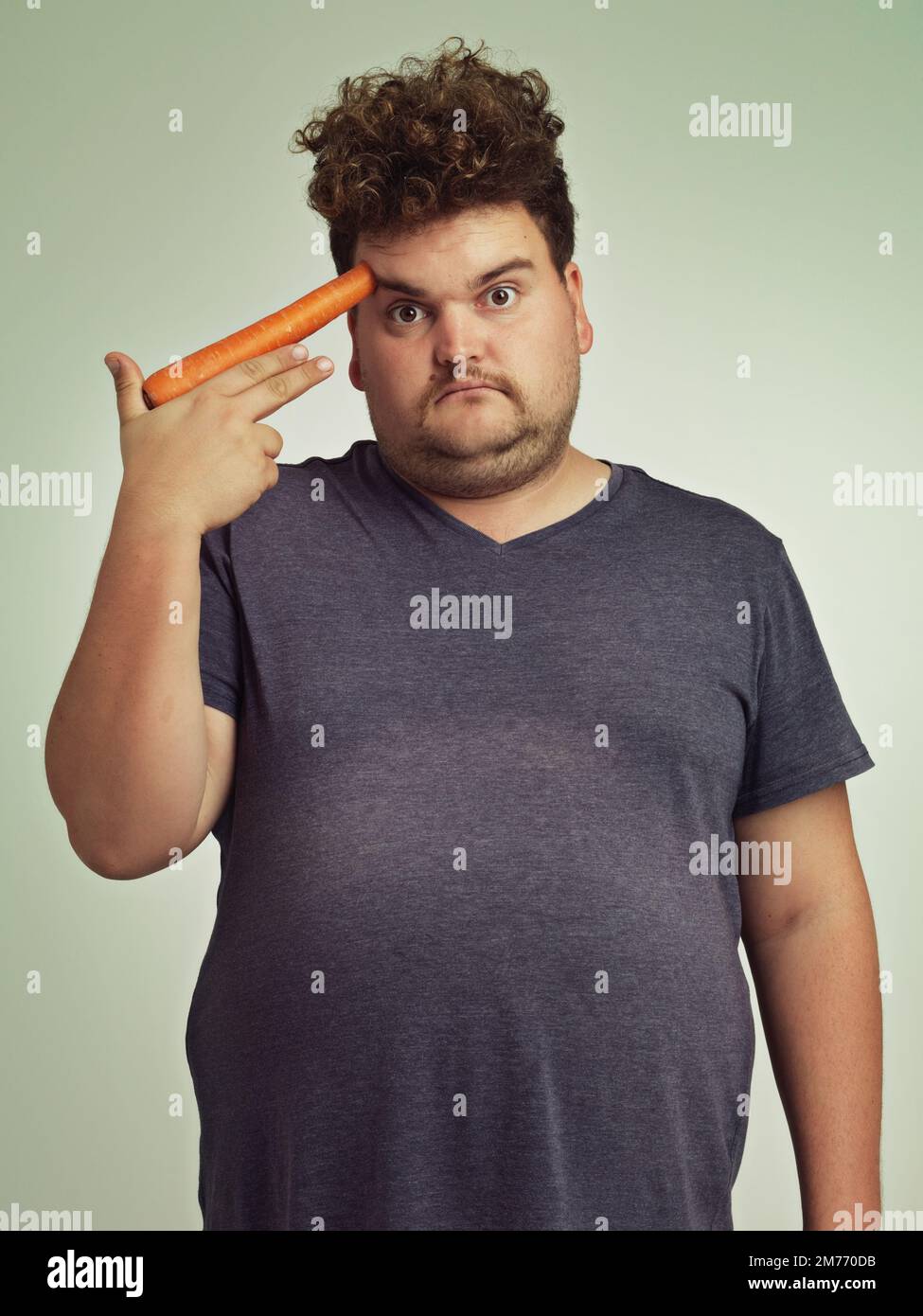 Wenn ich noch eine Karotte essen muss... ein übergewichtiger Mann, der eine Karotte an seinem Kopf hält. Stockfoto