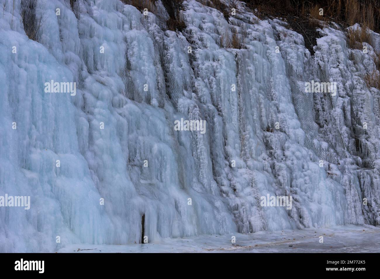 Wunderschöne Eisstrukturen eines gefrorenen Wasserfalls, hübsche Eiszapfen, die ein Interessantes Muster auf einem dunklen Felsen bilden und eine kalte und stimmungsvolle Atmosphäre schaffen Stockfoto