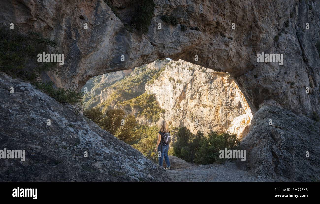 Eine Frau, die durch den Naturbogen Forat de la Vella im Naturpark Ports de Beseit, Katalonien, schaut Stockfoto