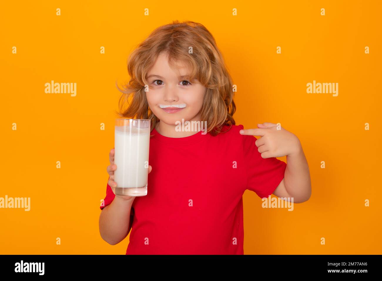 Gesundes Essen für Kinder. Ein Junge mit einem Glas Milch im Studio-Hintergrund. Süßes Kind in weißem Hemd, das ein Glas Milch auf isoliert auf gelb hält Stockfoto