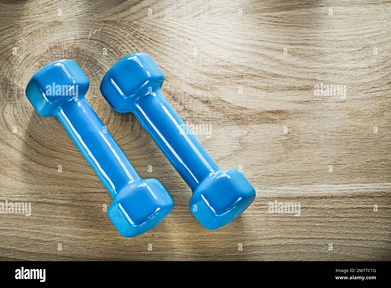 Ein Paar blaue Kurzhantel-Gewichte auf einem Holzbrett-Fitnesskonzept. Stockfoto