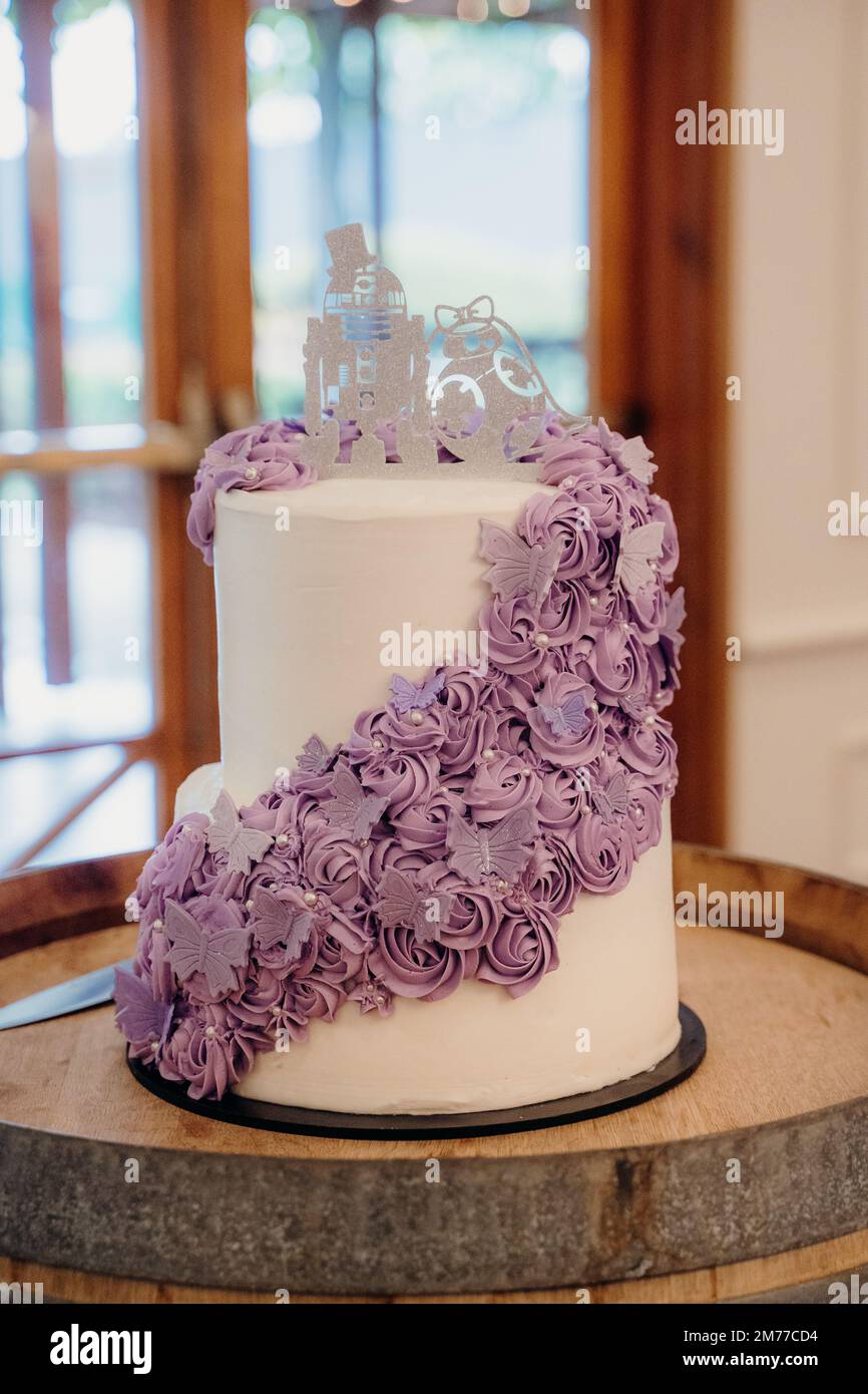 Eine vertikale Aufnahme einer weißen Hochzeitstorte mit violetten Blumen- und Schmetterlingsdekorationen Stockfoto