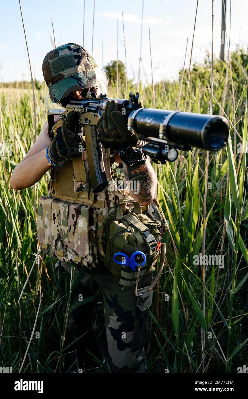 Ukrainische Militärdienerin mit einem Maschinengewehr in der Hand mitten auf dem Feld, automatisches Gewehr mit Schalldämpfer Nahaufnahme. Stockfoto