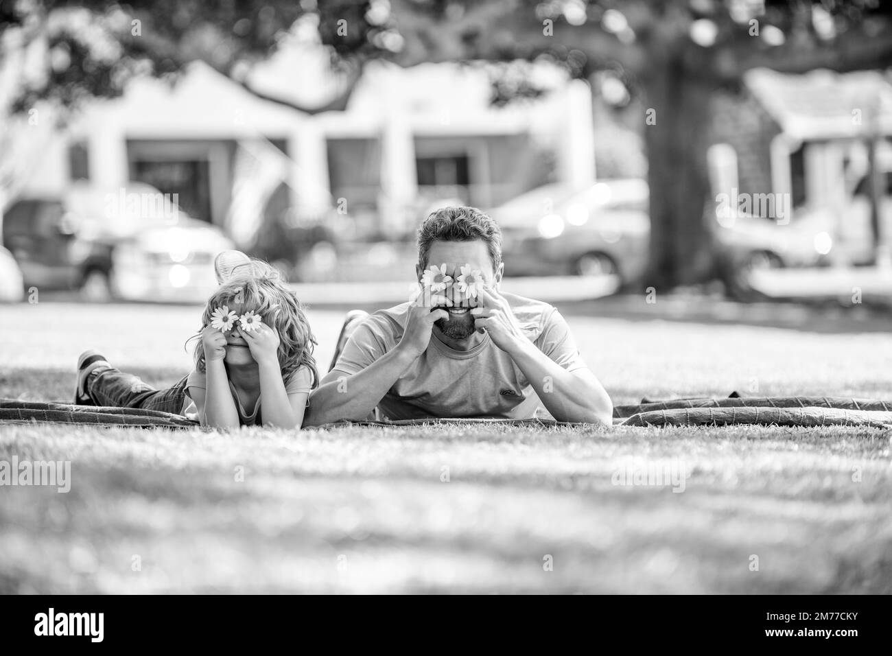 Glücklicher Vater mit Sohn spielen mit Blumen zusammen auf grünem Parkgras, Familie verbindet Stockfoto