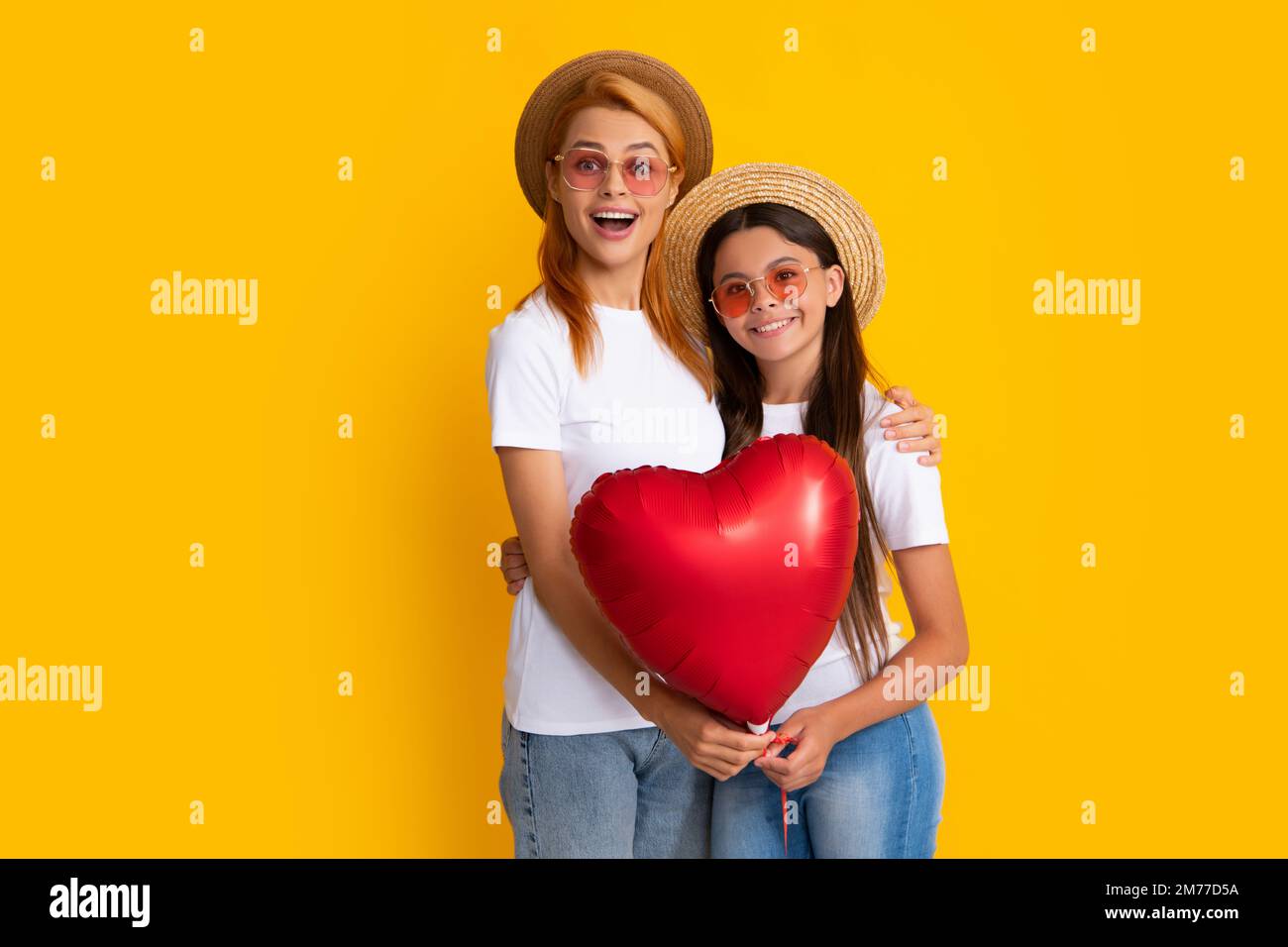 Ich liebe mom. Mutter und Tochter halten einen Herzballon. Glückliche Mutter und Tochter, die einen Liebesherz-Ballon auf gelbem Hintergrund halten. Stockfoto