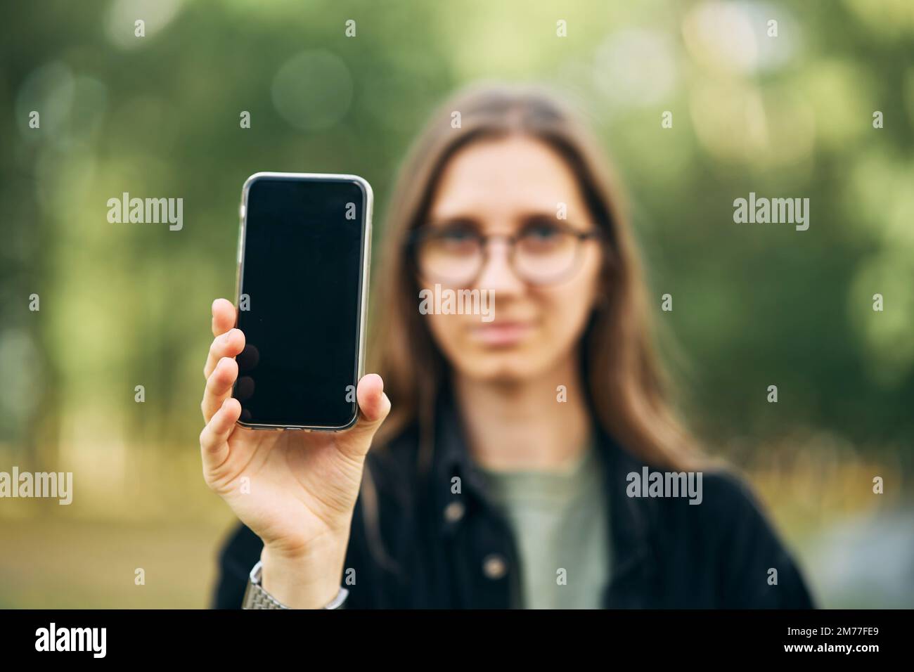 Ein junges Mädchen hält ein Telefon in der Hand und zeigt es auf dem Bildschirm in Richtung Kamera Stockfoto