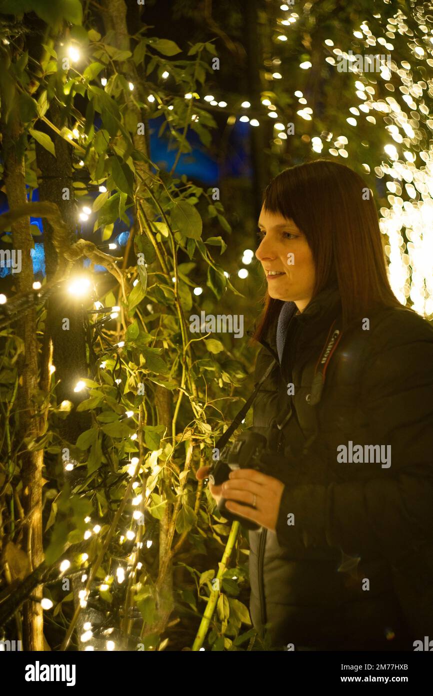 Frau genießt magische Weihnachtslichter im Winterlaub bei festlicher Gartenattraktion Stockfoto