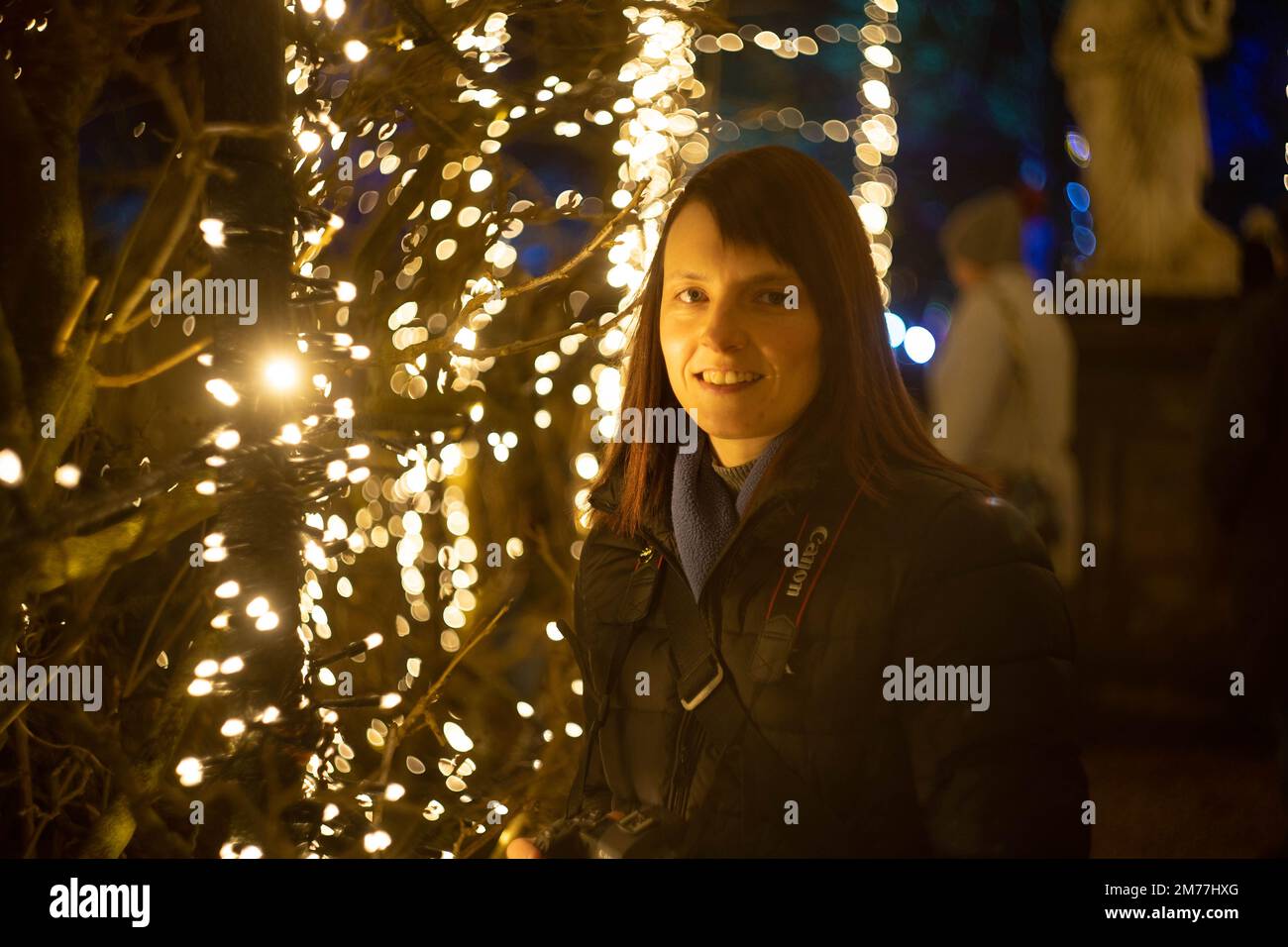Eine junge Frau lächelt zwischen funkelnden Weihnachtslichtern bei festlicher Abendfeier Stockfoto