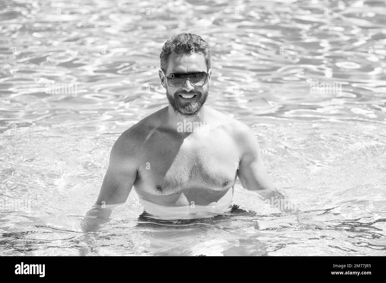 Fröhlicher muskulöser Mann in einer Brille, der im Sommer im Pool schwimmend ist Stockfoto